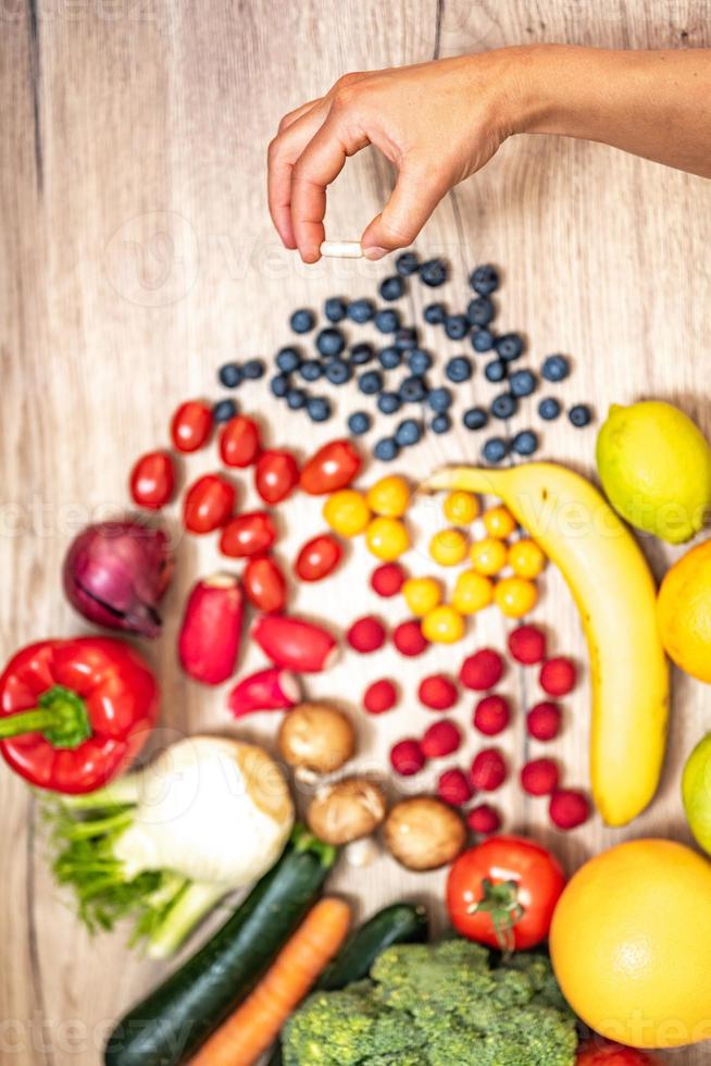 mano sujetando suplementos alimenticios sobre verduras y frutas para un estilo de vida saludable foto