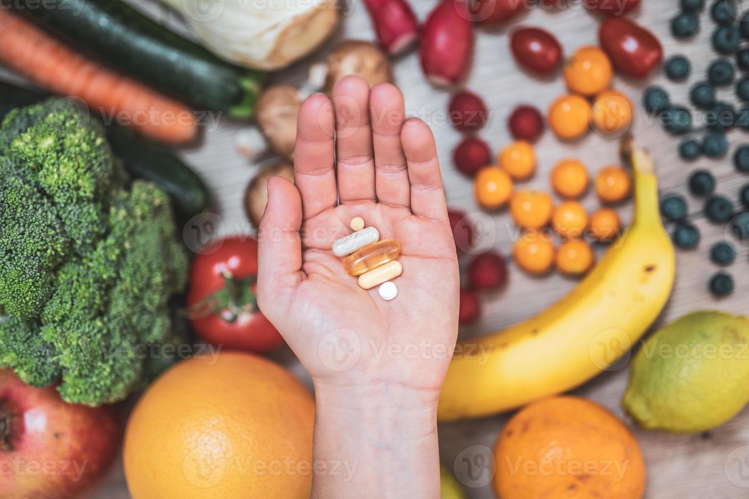 mano sujetando suplementos alimenticios sobre verduras y frutas para un estilo de vida saludable foto
