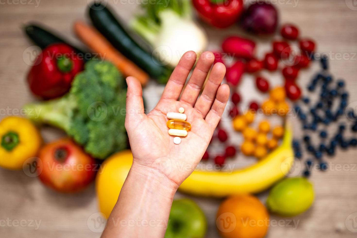 mano sujetando suplementos alimenticios sobre verduras y frutas para un estilo de vida saludable foto