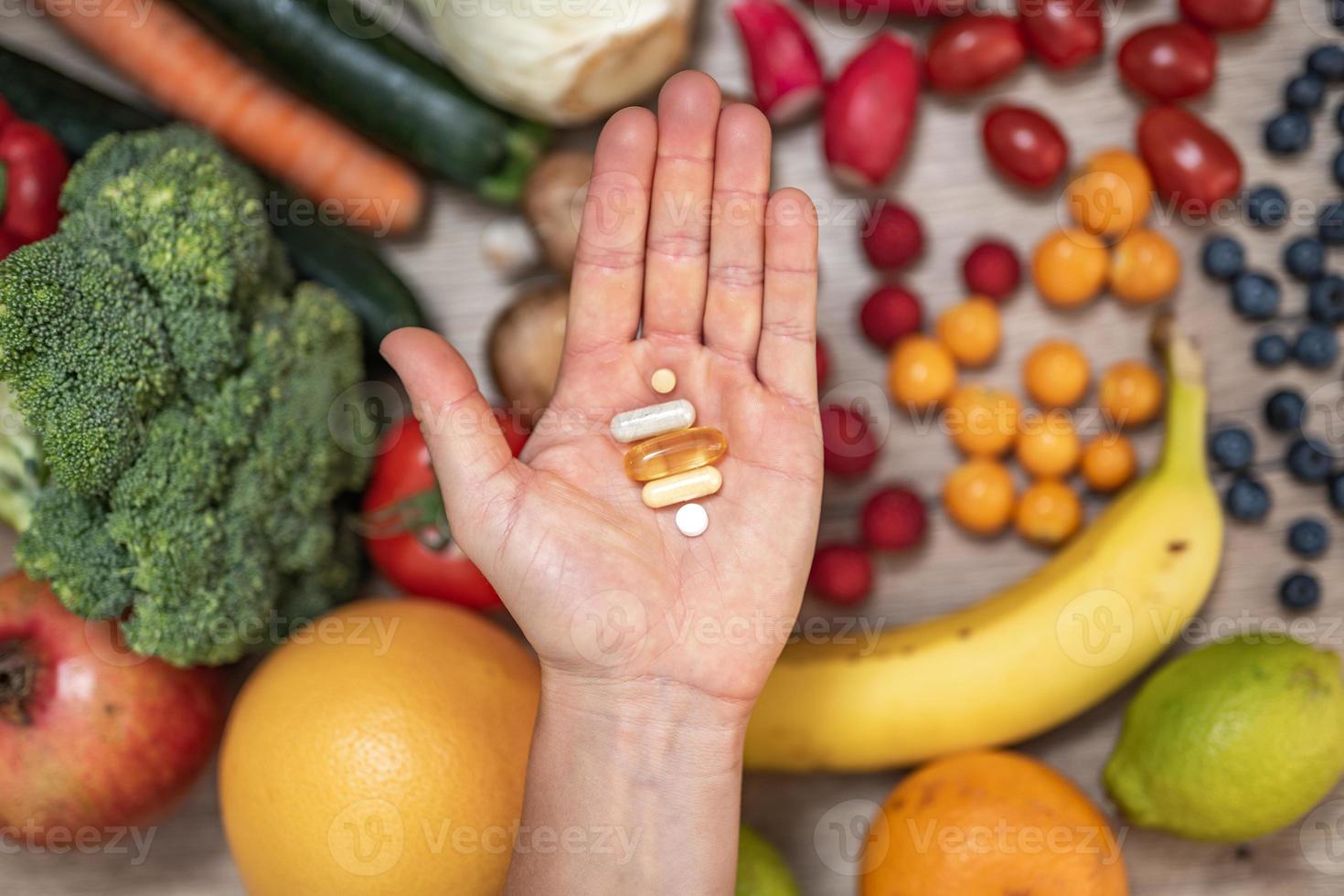 mano sujetando suplementos alimenticios sobre verduras y frutas para un estilo de vida saludable foto