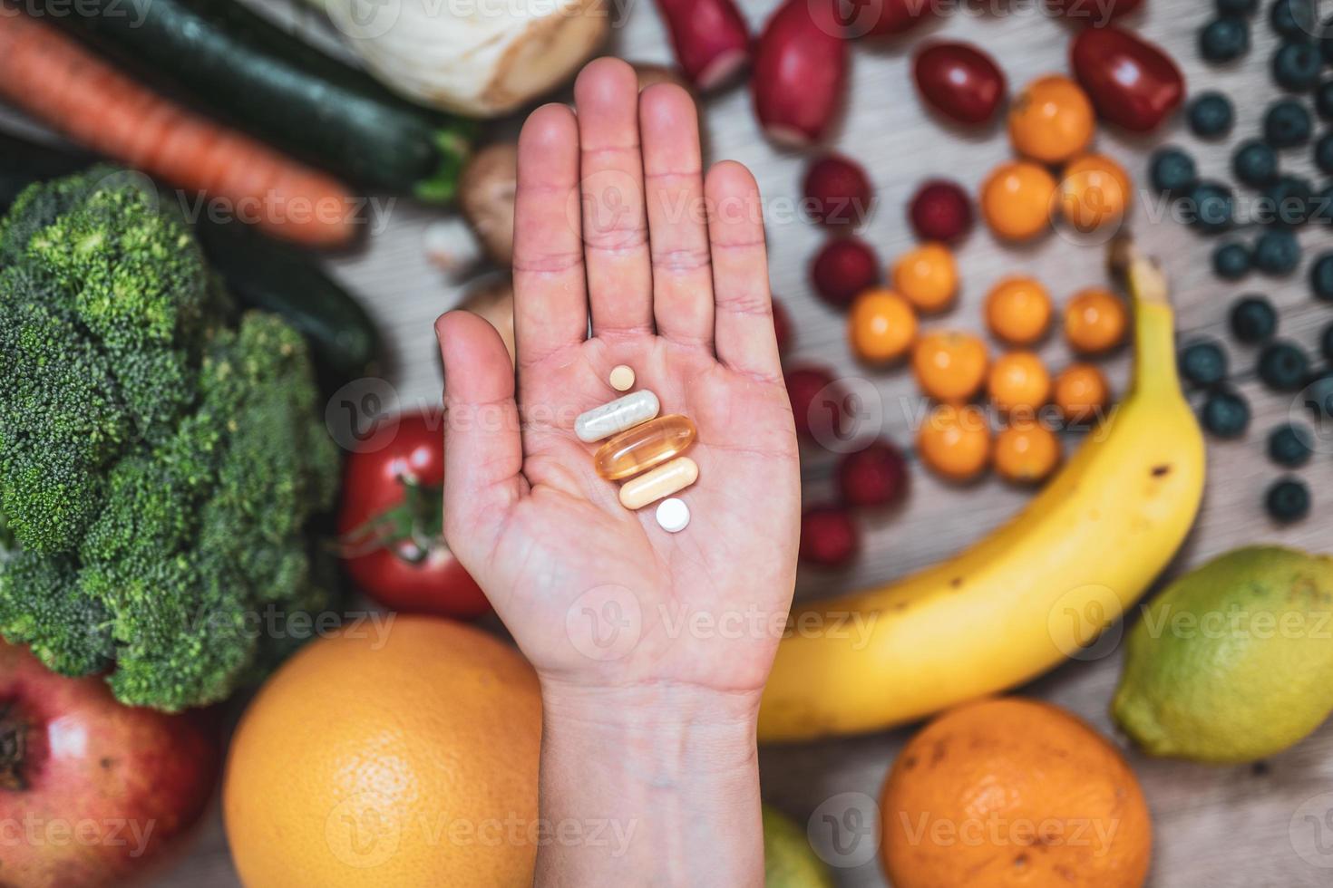 mano sujetando suplementos alimenticios sobre verduras y frutas para un estilo de vida saludable foto