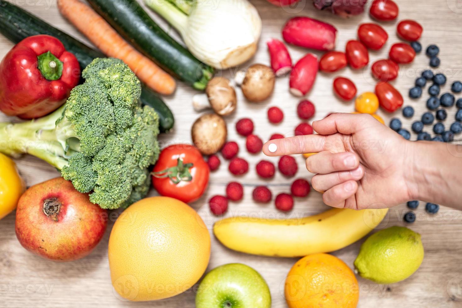 mano sujetando suplementos alimenticios sobre verduras y frutas para un estilo de vida saludable foto