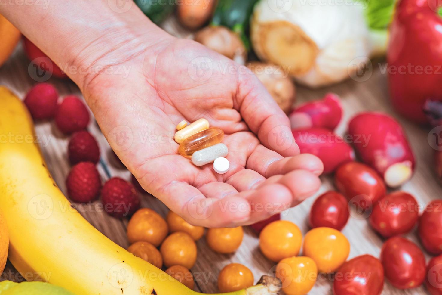 mano sujetando suplementos alimenticios sobre verduras y frutas para un estilo de vida saludable foto