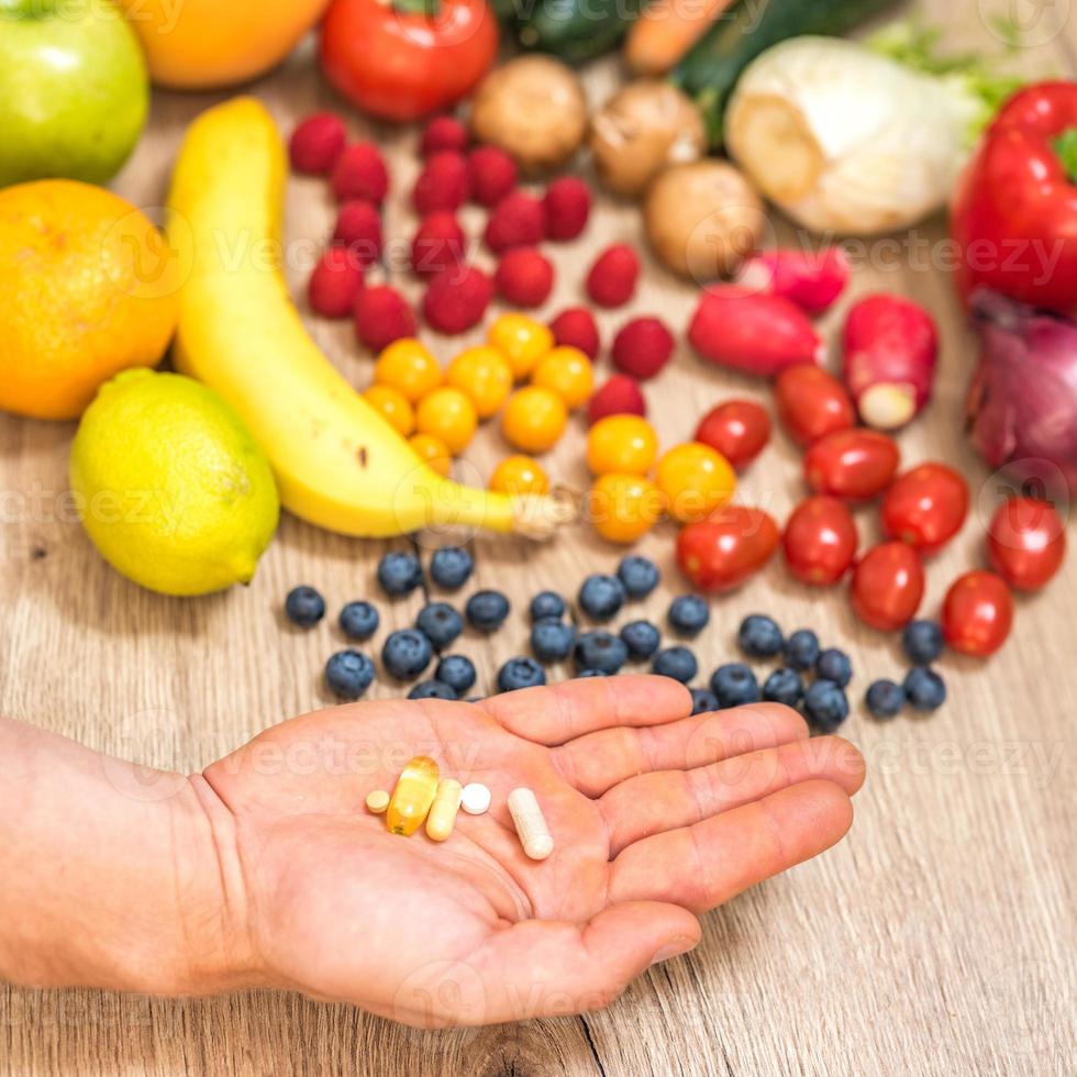 Hand holding food supplements over vegetables and fruits for a healty lifestyle photo