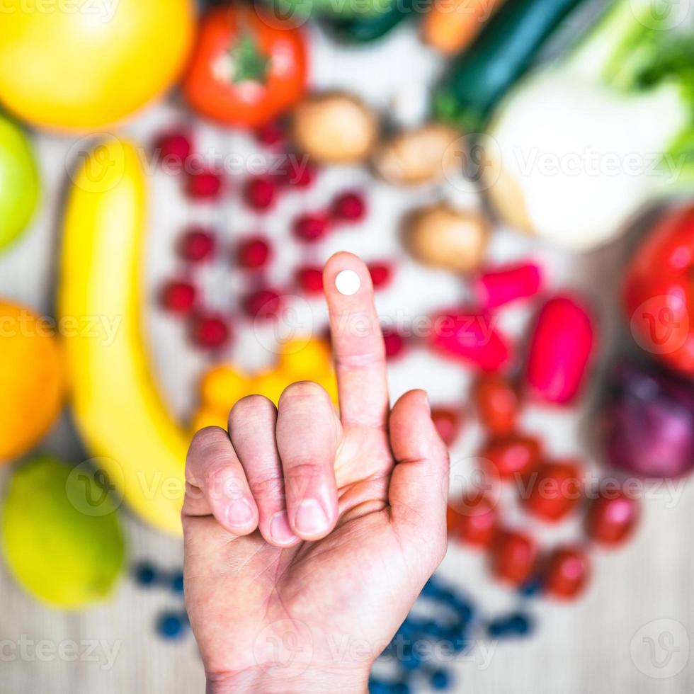 mano sujetando suplementos alimenticios sobre verduras y frutas para un estilo de vida saludable foto