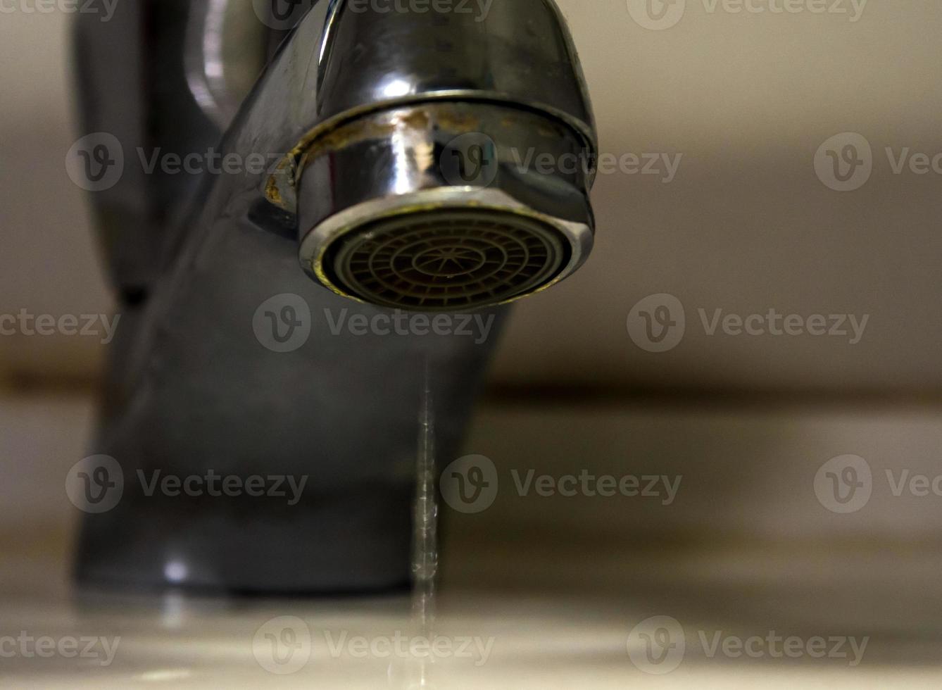 Leaking water drops from old rust and stained faucet photo