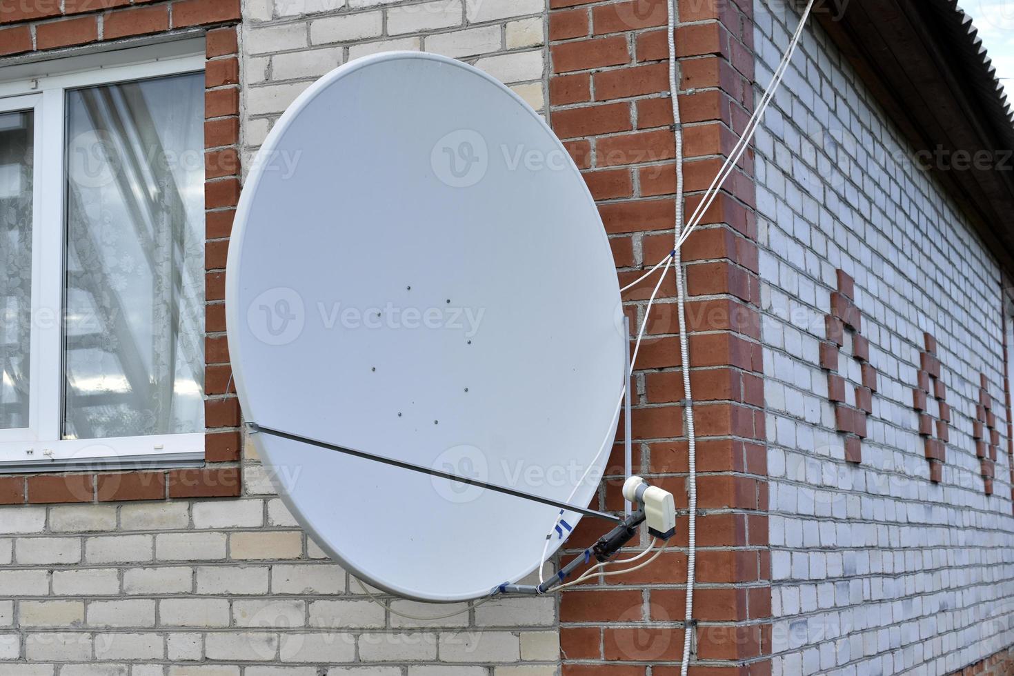 Parabolic antenna on a brick private house in summer photo