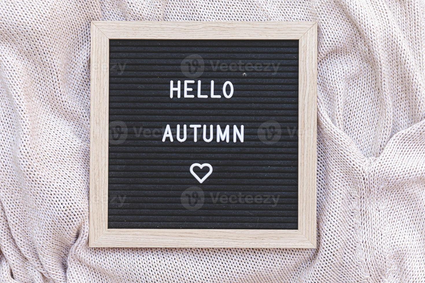Autumnal Background. Black letter board with text phrase Hello Autumn lying on white knitted sweater. Top view, flat lay. Thanksgiving banner. Hygge mood cold weather concept photo