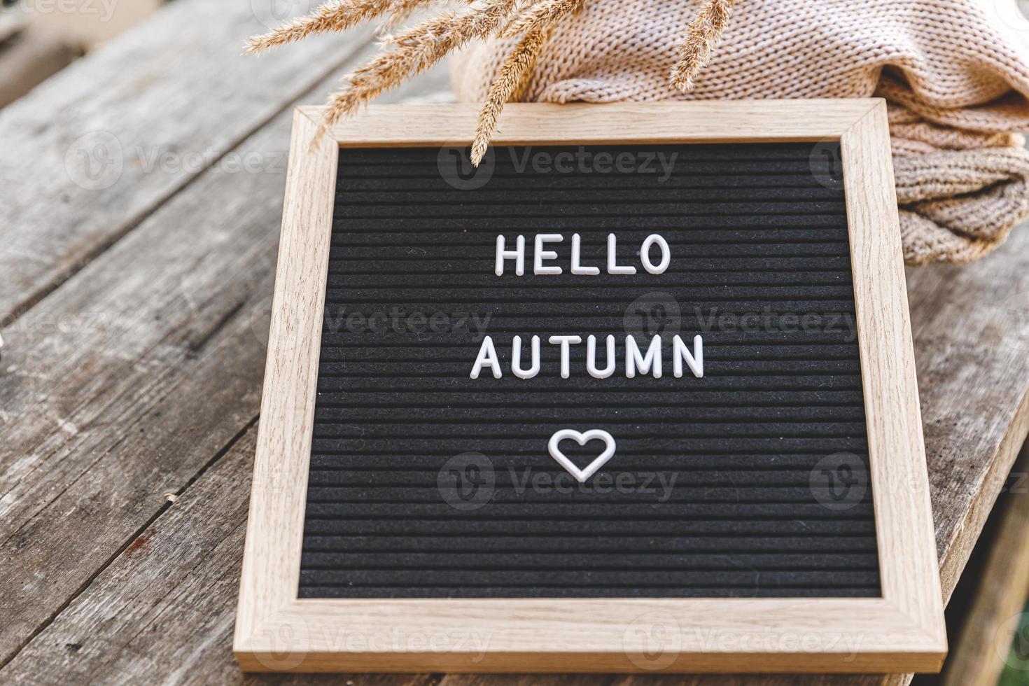 Autumnal Background. Black letter board with text phrase Hello Autumn and dried plant lying on wooden palnks. Top view, flat lay. Thanksgiving banner. Hygge mood cold weather concept photo