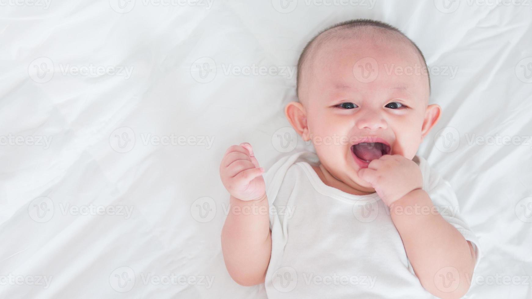 Portrait of cute asian newborn baby lying play on white bed look at camera with laughing smile happy face. Innocent little new infant adorable. Parenthood and Mother Day concept. photo