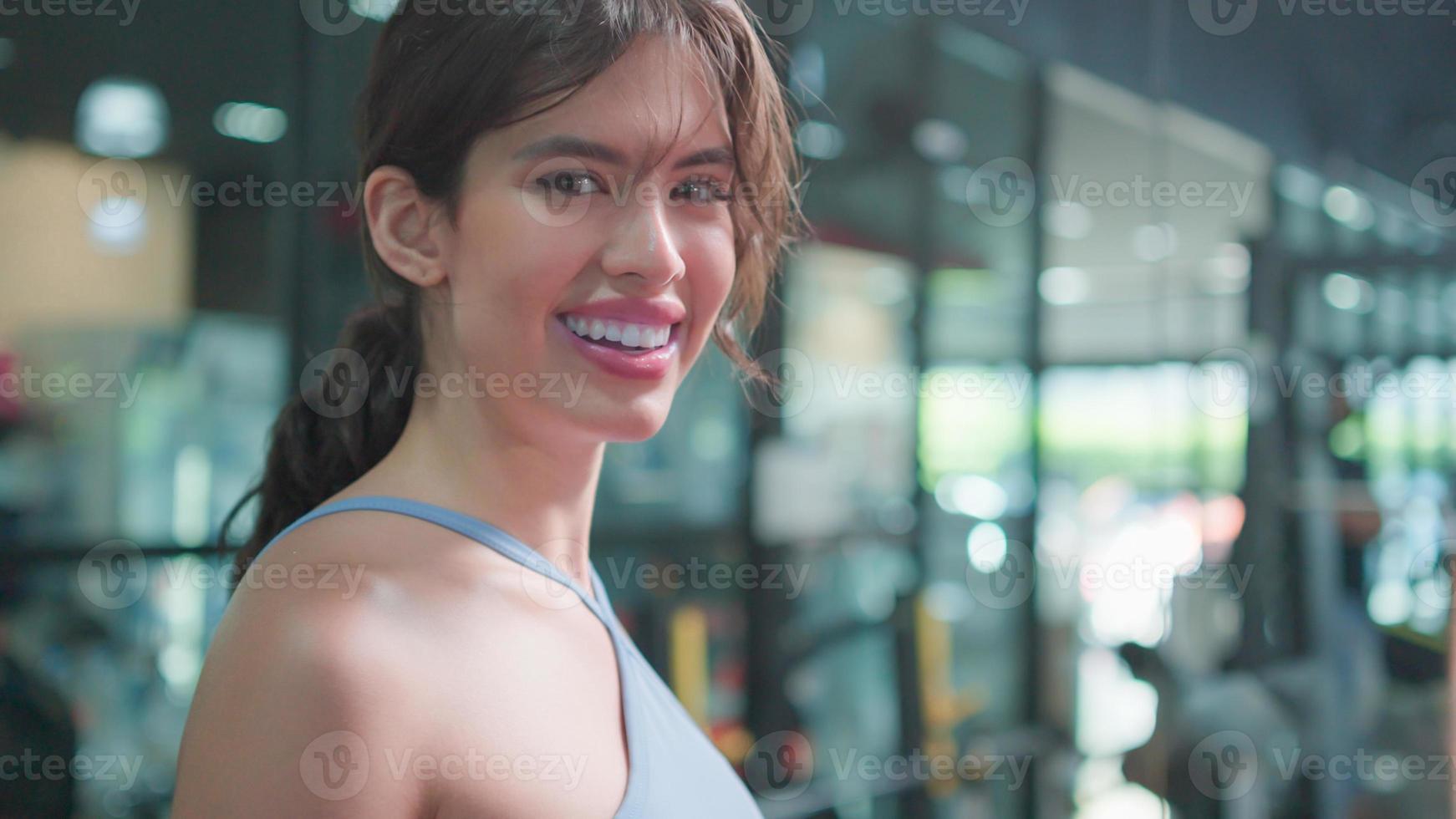 retrato de primer plano de una hermosa joven asiática durante la mirada a la cámara con cara de sonrisa feliz. atleta de fitness hermosa chica con ropa deportiva posando en el gimnasio. concepto de estilo de vida saludable. foto