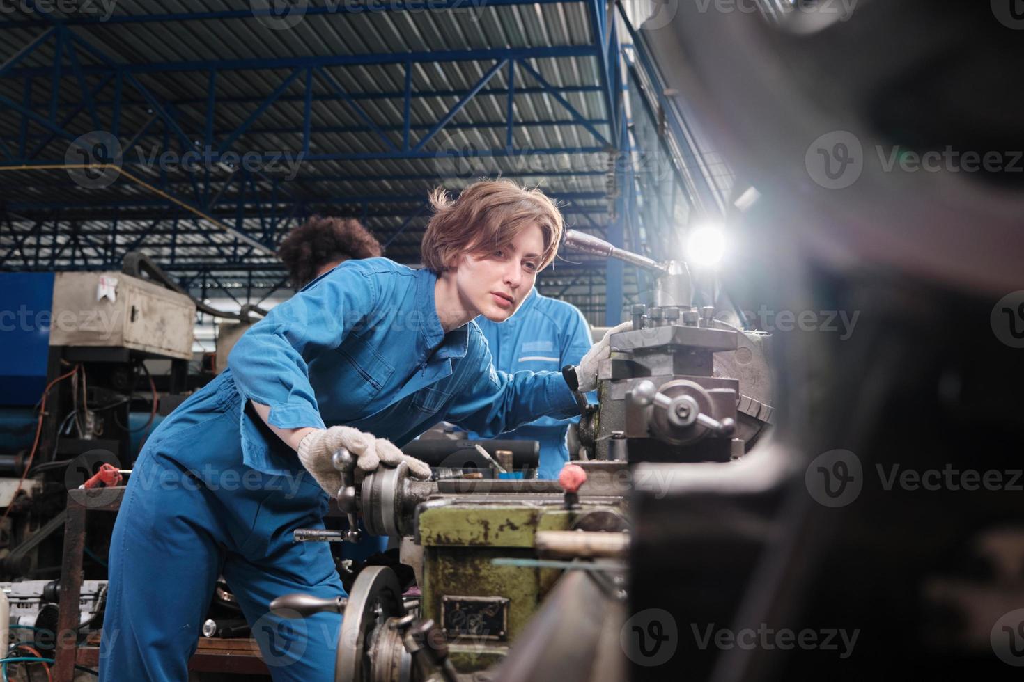 Professional young White female industry engineer worker works in safety uniform with metalwork precision tools, mechanical lathe machines, and spare parts workshop in the steel manufacturing factory. photo
