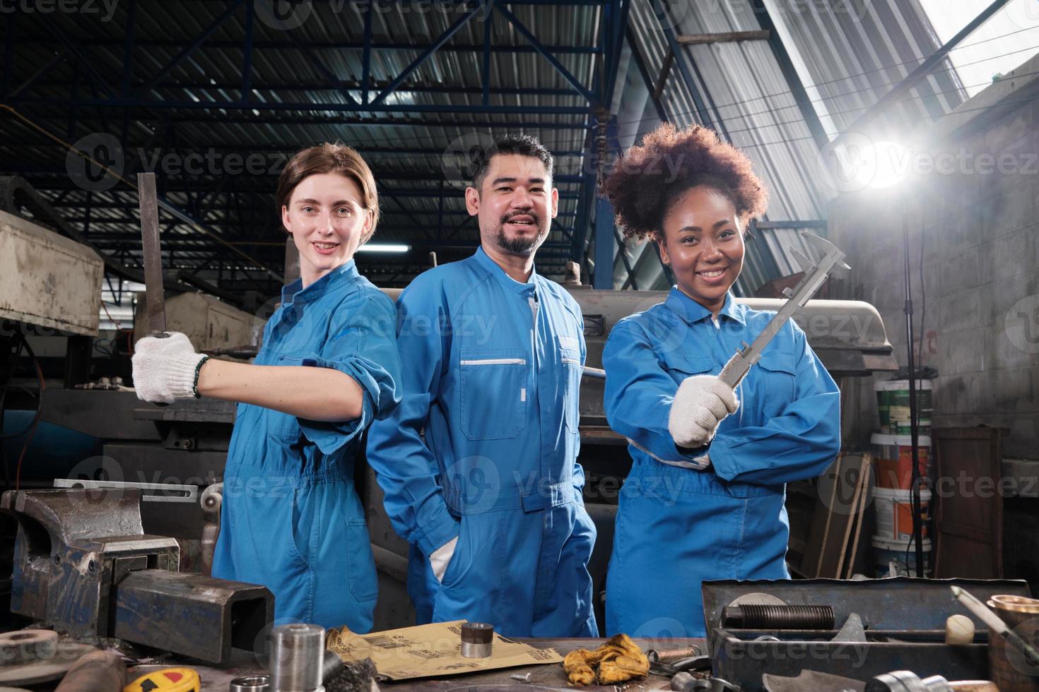 Multiracial industry workers in safety uniforms collaborate with unity, act with tools, and express happy work together with smile and cheerful in mechanical factory, professional engineer occupation. photo