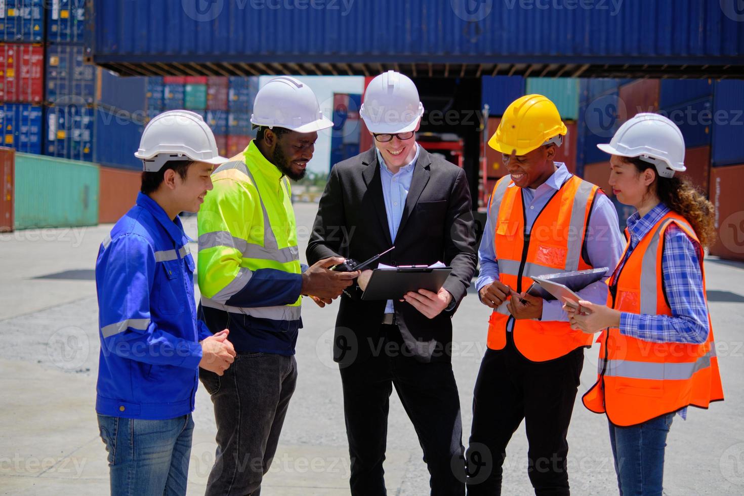 Group of multiracial workers in safety uniforms and hardhats work at logistics terminal dock with stacks of containers, loading control, and management shipping goods, cargo transportation industry. photo