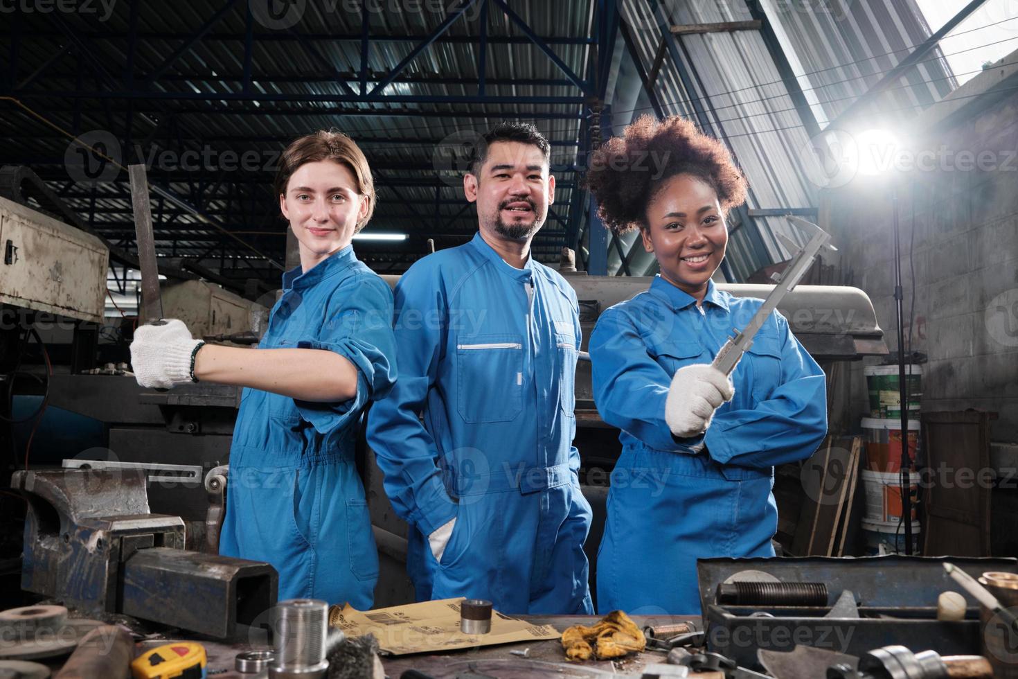 Multiracial industry workers in safety uniforms collaborate with unity, act with tools, and express happy work together with smile and cheerful in mechanical factory, professional engineer occupation. photo