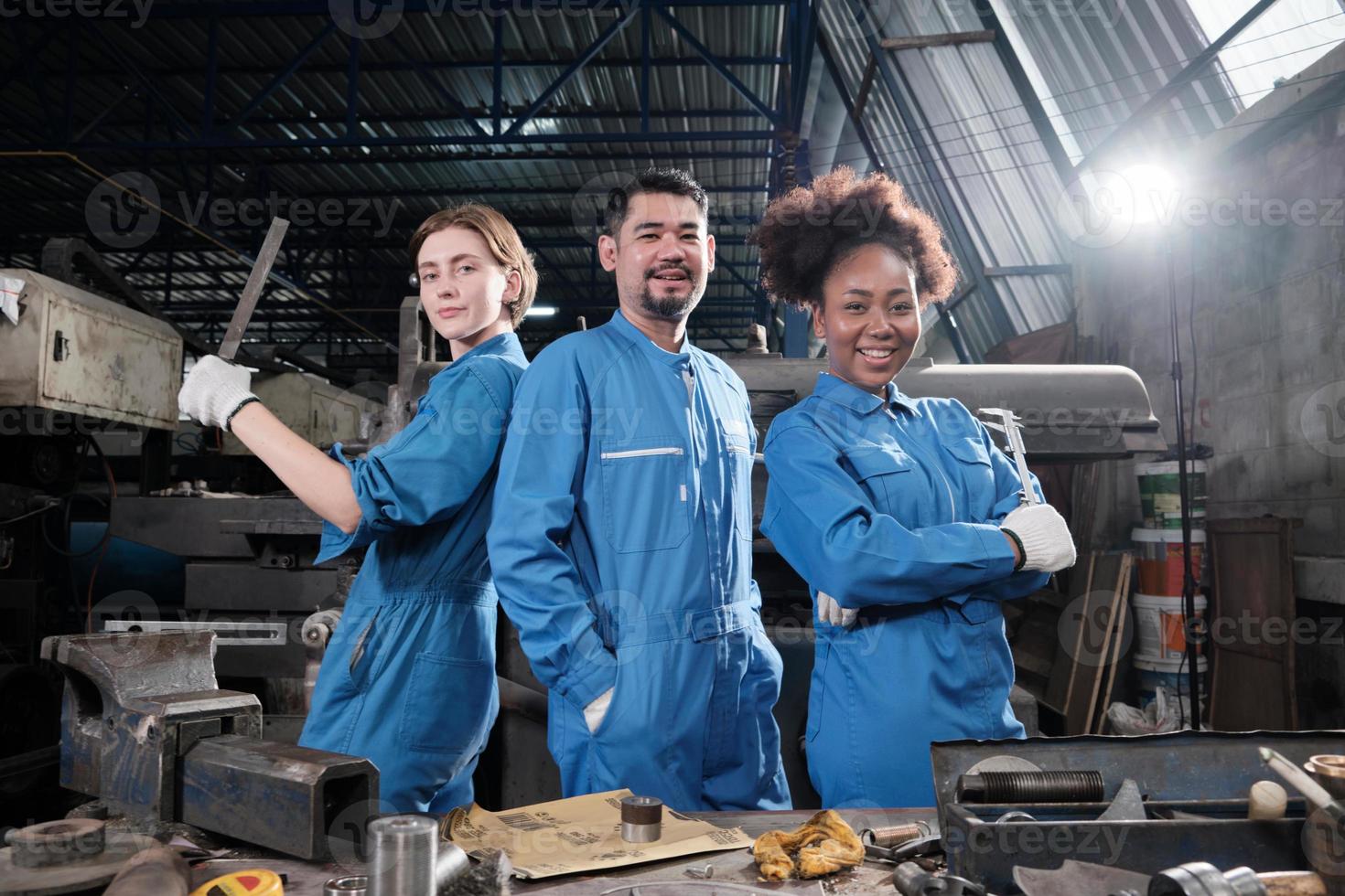 Multiracial industry workers in safety uniforms collaborate with unity, act with tools, and express happy work together with smile and cheerful in mechanical factory, professional engineer occupation. photo