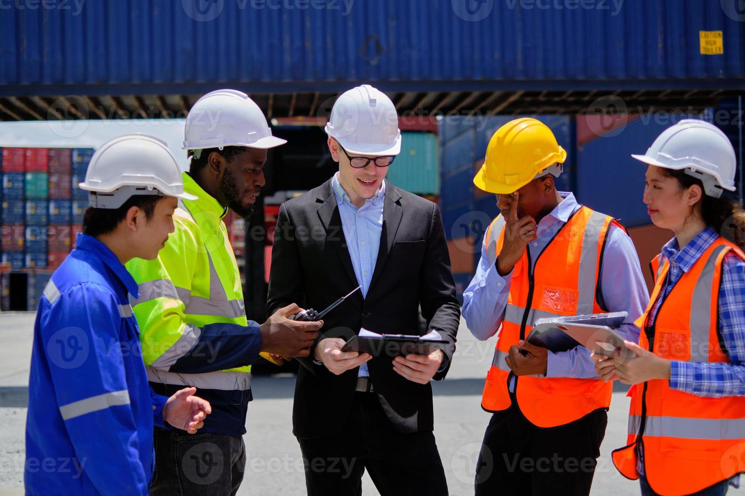 Group of multiracial workers in safety uniforms and hardhats work at logistics terminal dock with stacks of containers, loading control, and management shipping goods, cargo transportation industry. photo