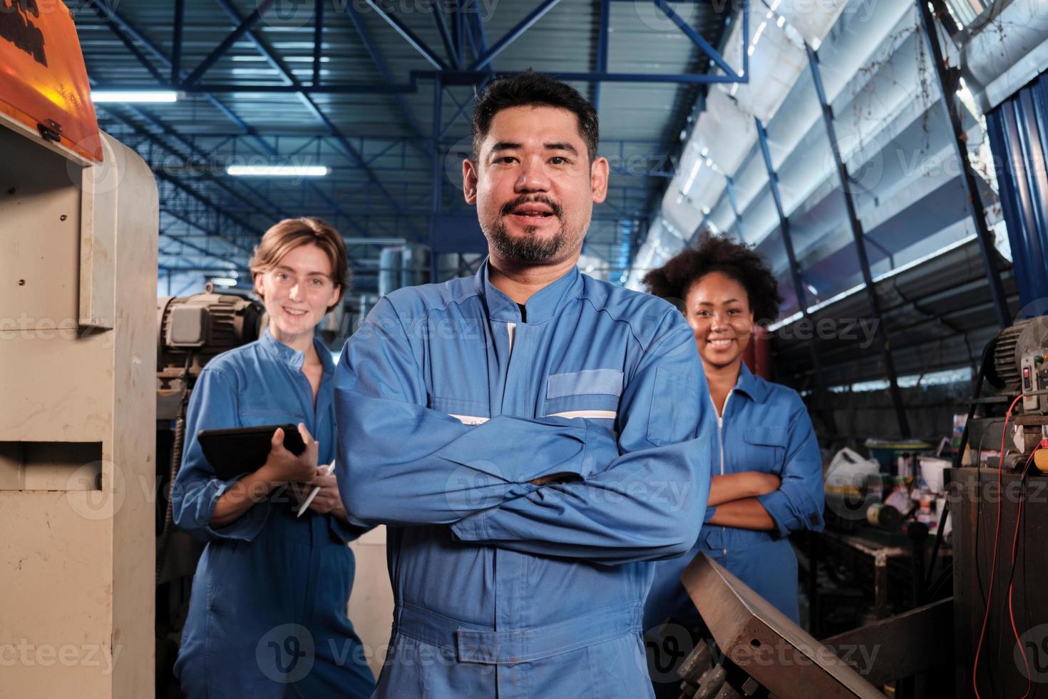 Multiracial industry workers in safety uniforms collaborate with unity, arms crossed, and express happy work together with smile and cheerful in mechanical factory, professional engineer occupation. photo