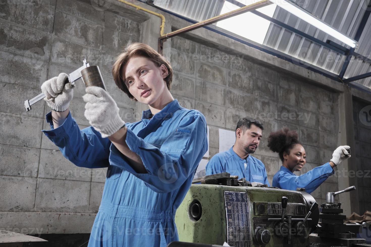 Young Caucasian female industry worker works with metalwork precision tools, lathe machines, and spare parts workshop with multiracial team in manufacturing factory, professional mechanical engineers. photo
