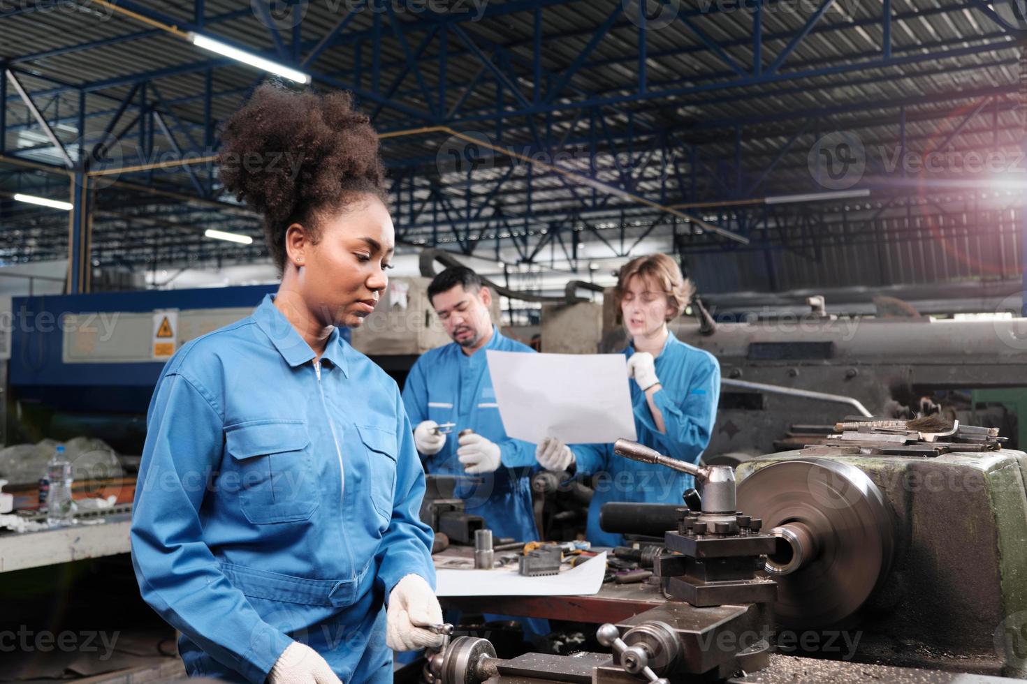 A professional African American female industry engineer worker works in safety uniform with metalwork precision tools, mechanical lathe machines, and spare parts workshop in a manufacturing factory. photo