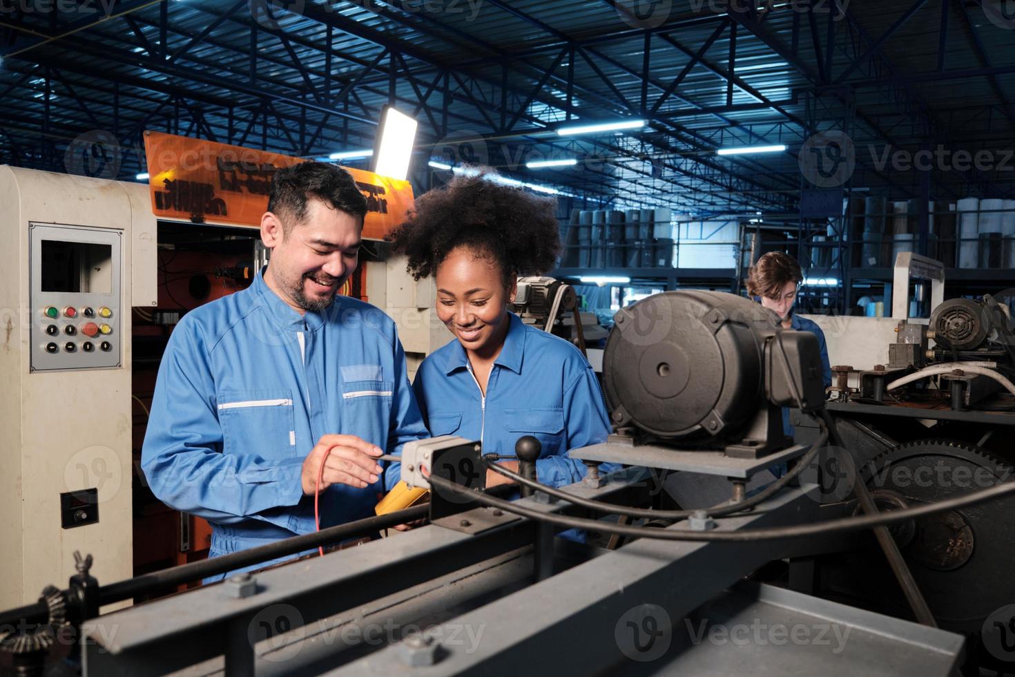 Asian male and female African American engineers in safety uniform work by inspecting machines' voltage current, checking, and maintaining at manufacture factory, electric system service occupations. photo