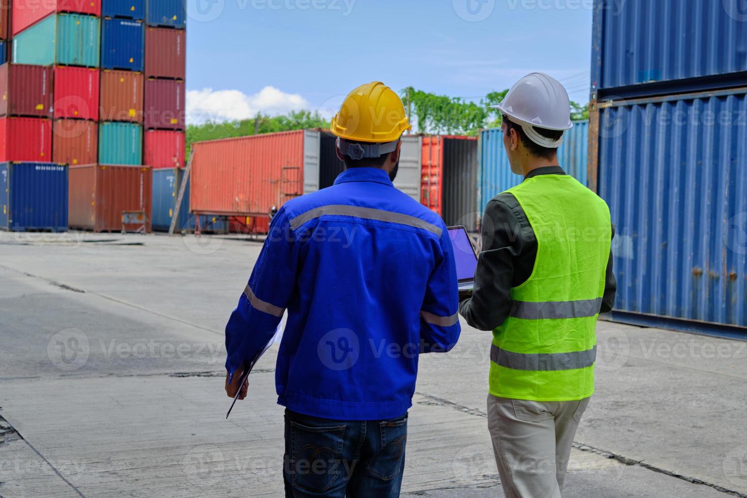 Two professional male workers in safety uniforms and hard hats work and inspect a logistics terminal with many stacks of containers, loading control shipping goods for cargo transportation industry. photo