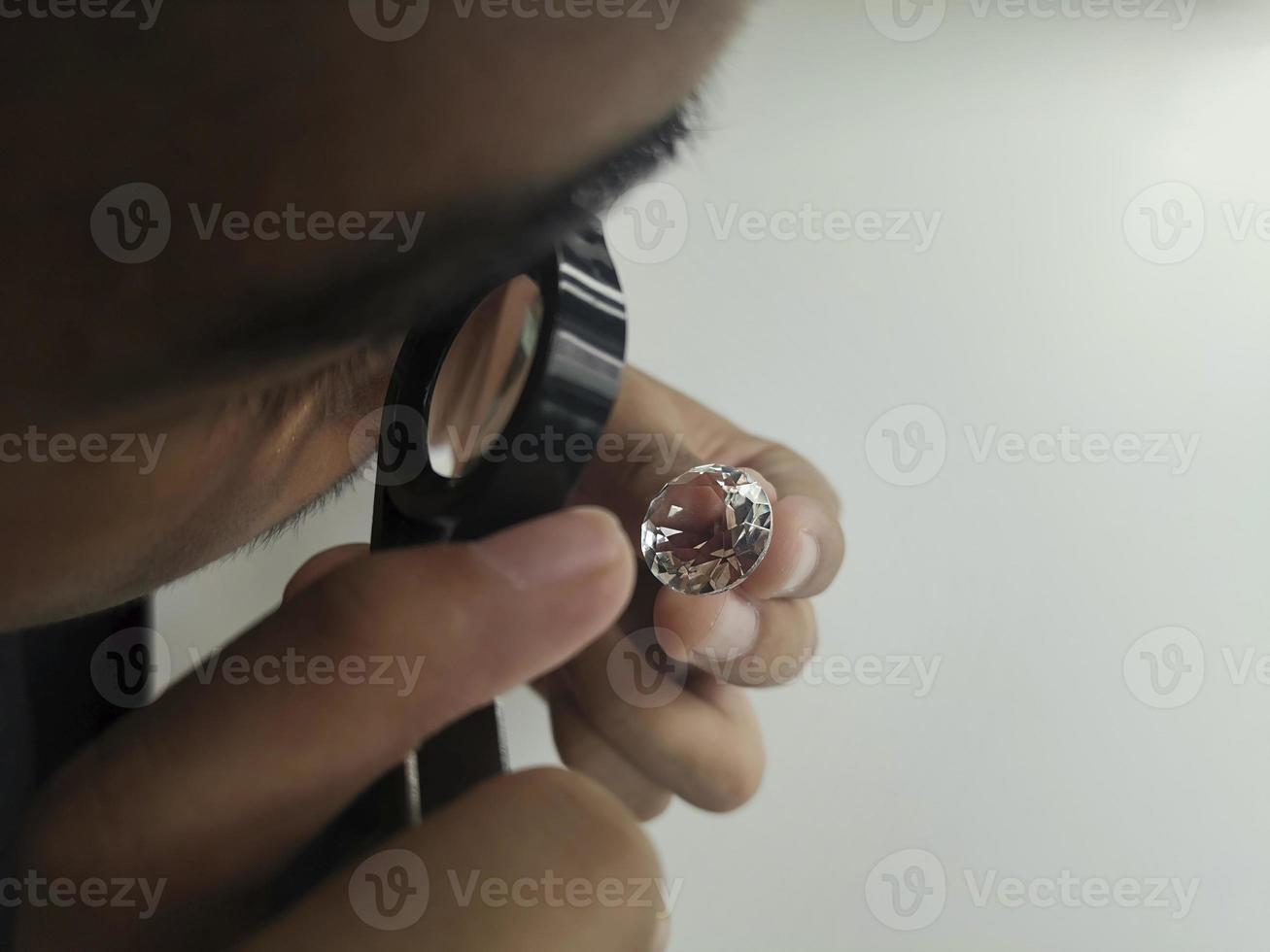 Man jeweller examines polished diamond through magnifier. Buyer checking diamond. Cut and polished diamond. Diamond jewellery under grading. Jeweller looking through loupe photo