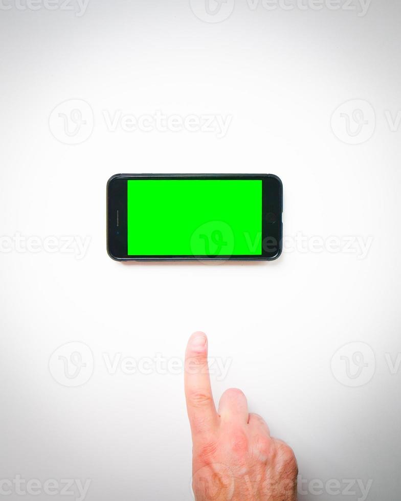 dedo de la mano masculina hasta la pantalla verde del teléfono inteligente en las cortinas de fondo blanco. espacio en blanco aislado copypaste fondo de smartphone maqueta foto