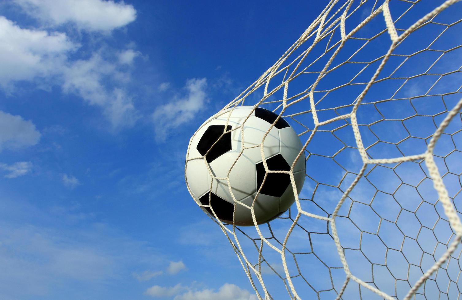 símbolo de éxito y victoria para el balón de fútbol clásico tiene color blanco y negro entrando en la red de gol después de disparar en el juego con un fondo de cielo azul. concepto de éxito. foto
