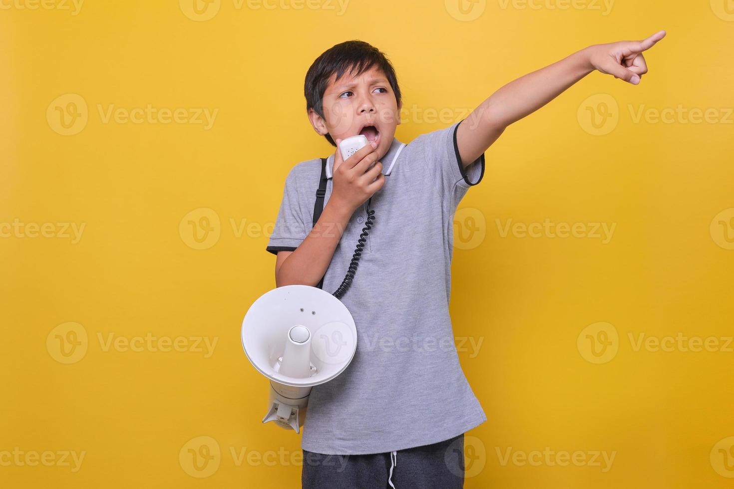 Cute Asian boy shouting on megaphone while pointing out index finger againts yellow background photo