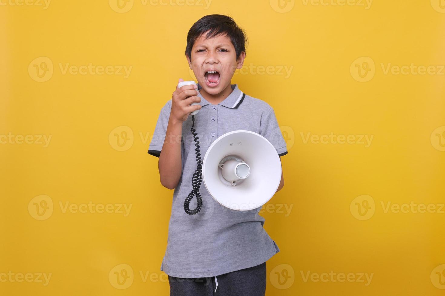 Cute Asian boy yelling on megaphone againts yellow background photo