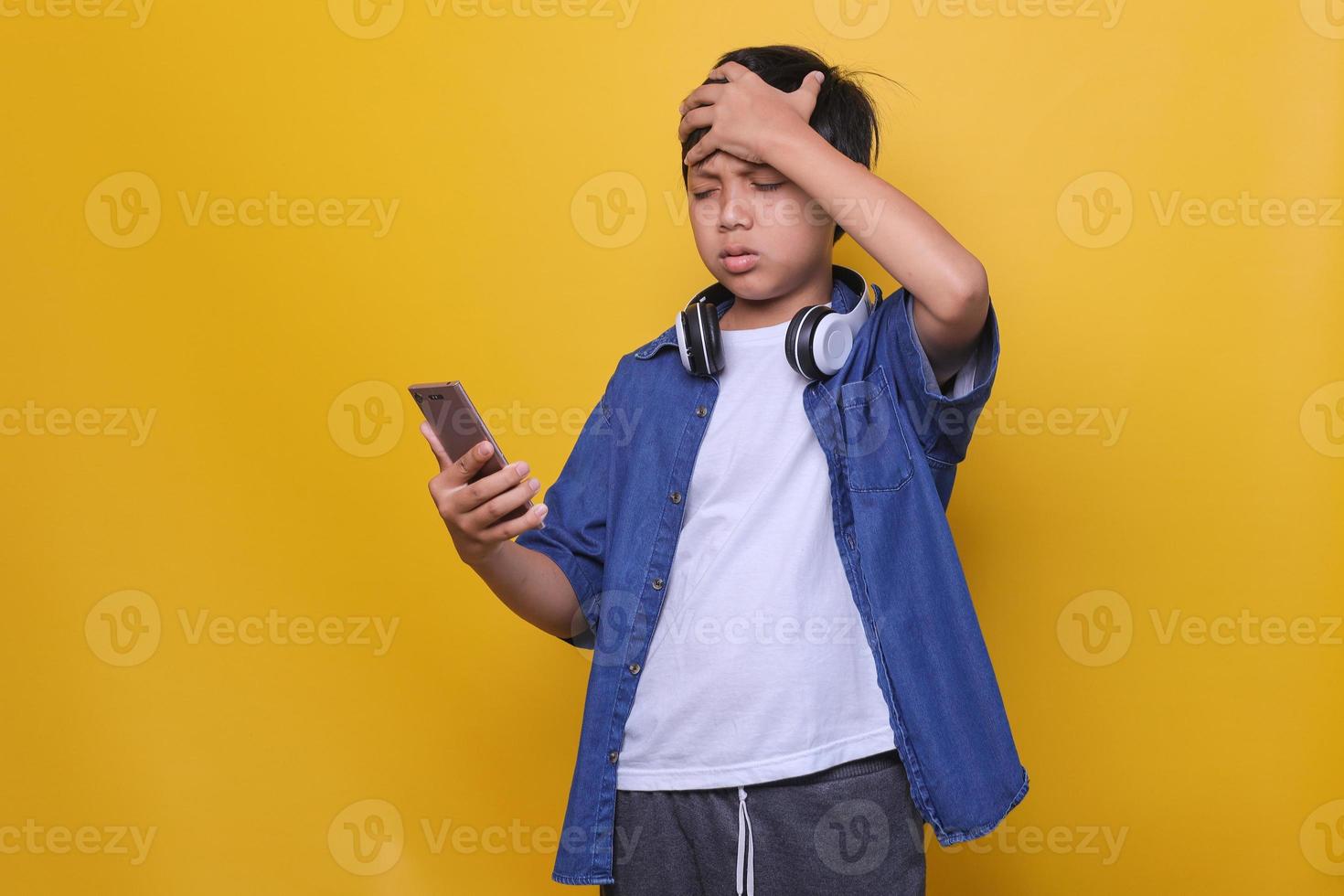 niño asiático usando un teléfono inteligente y mirando la pantalla del teléfono estresado con la mano en la cabeza, sintiéndose triste y preocupado. miedo y malestar por error. foto