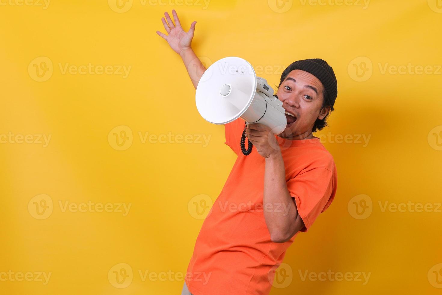 Asian cheerful casual guy isolated on yellow background speaking through a megaphone. photo