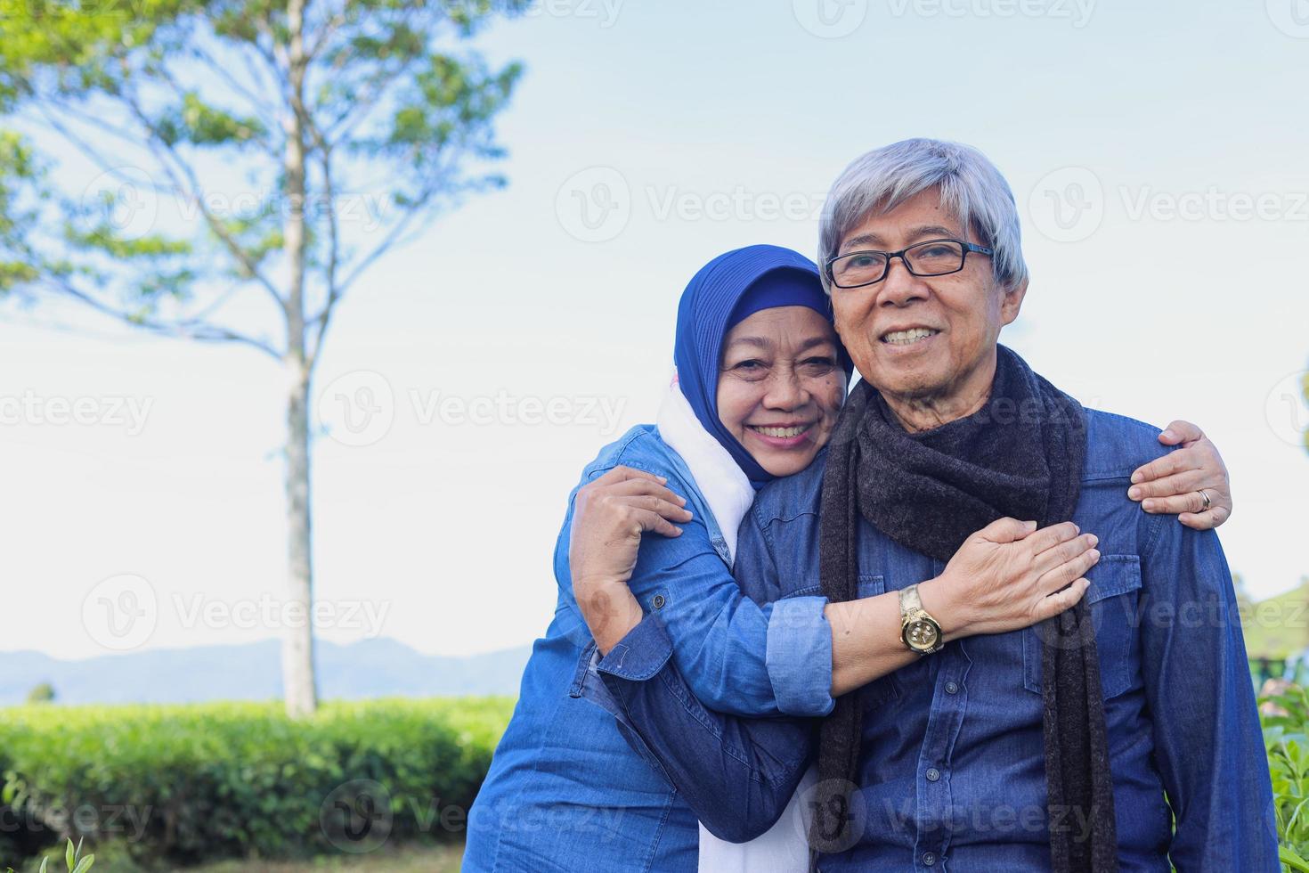 Elderly couple. Joyful senior romantic couple smiling to the camera at tea plantation. Grandmother hug grandfather. photo