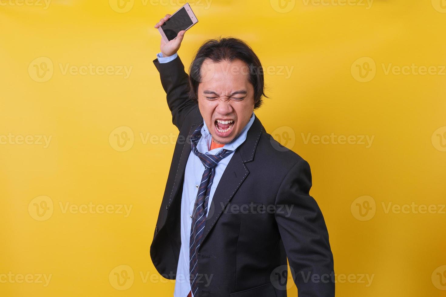 hombre de negocios enojado. hombre de negocios estresado experimentado que se siente muy enojado mientras tira su teléfono inteligente. foto de estudio sobre fondo amarillo.