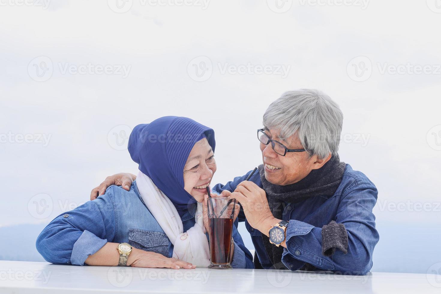 Romantic senior couple sitting and drinking tea together in one glass. Happy retired couple. photo