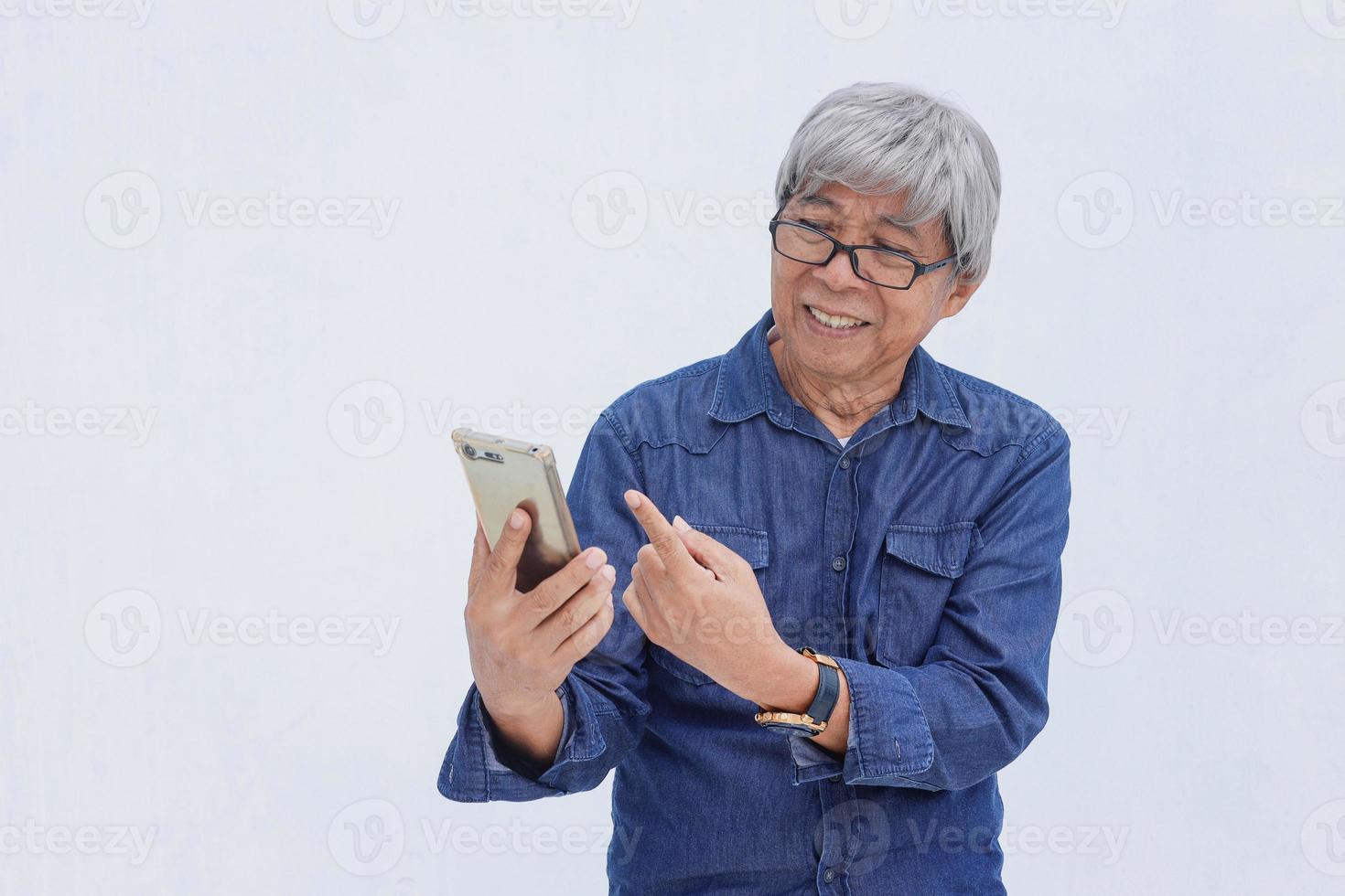 retrato de un anciano asiático con un estilo informal de mezclilla señalando con el dedo al teléfono inteligente. concepto y estilo de vida senior en línea y redes sociales foto