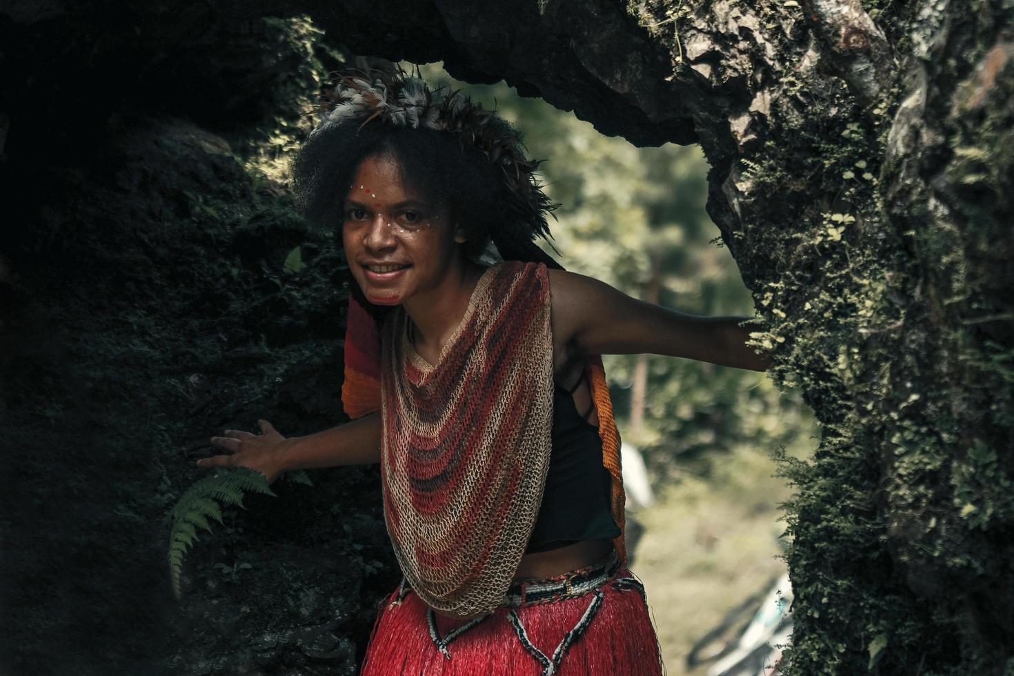 exótica joven papua niña de la tribu dani en ropa tradicional con corona de plumas está sonriendo y jugando en la cueva foto