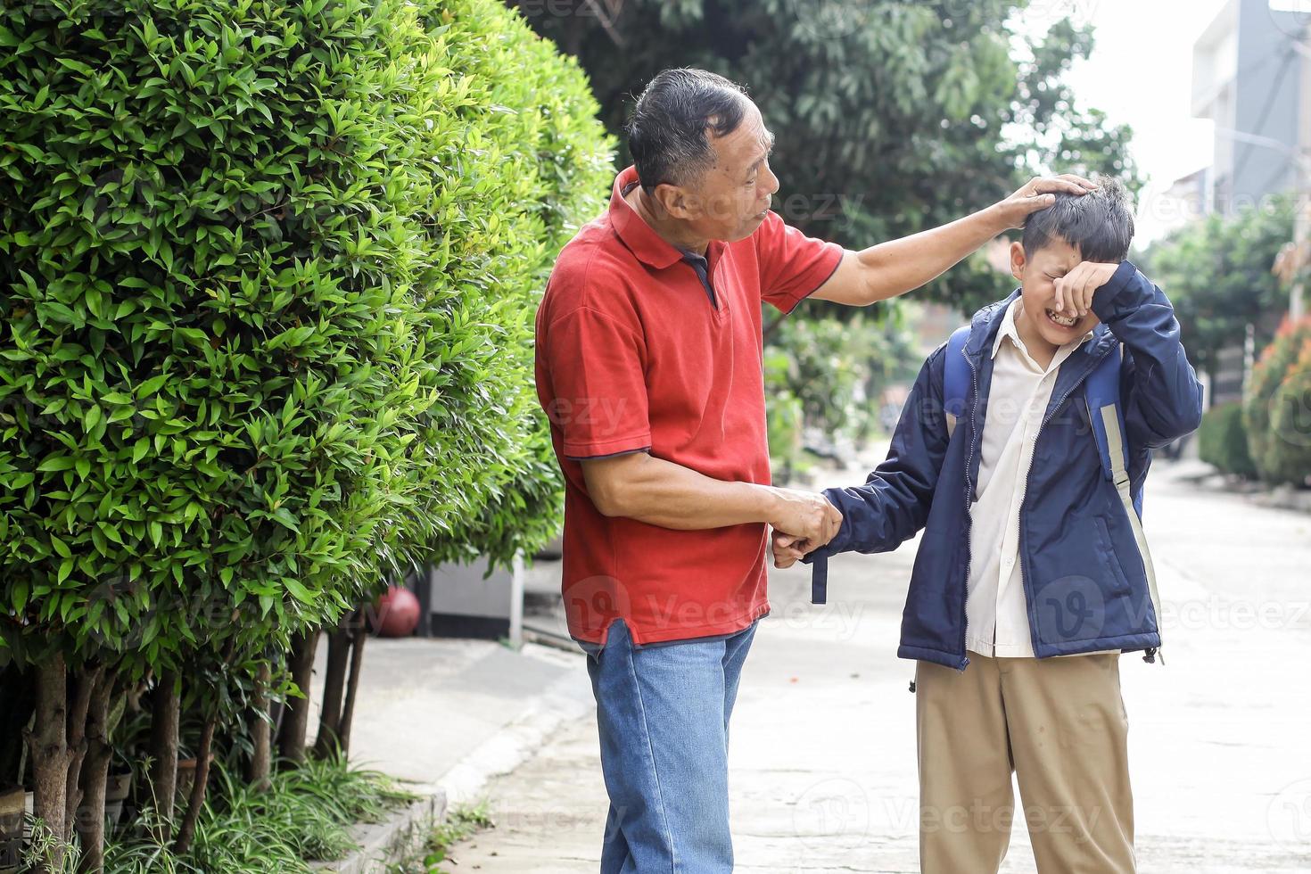el abuelo trata de consolar a su nieto que llora después de la escuela acariciando la cabeza. concepto de crianza y actividad familiar. foto