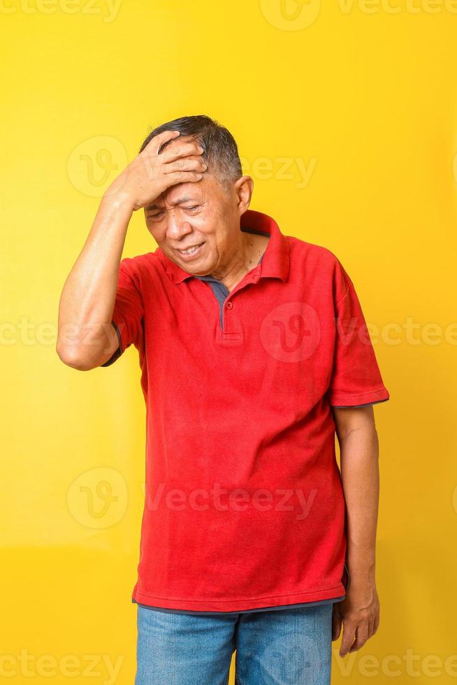 Health care, stress, old age and people concept - Asian senior man suffering from headache isolated on yellow background. photo