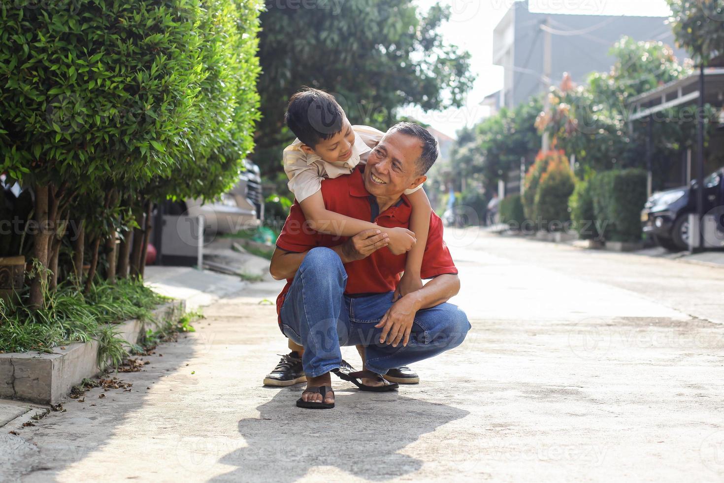 Asian school boy hug his grandfather from behind at the house yard. Parenting and family activity concept. photo