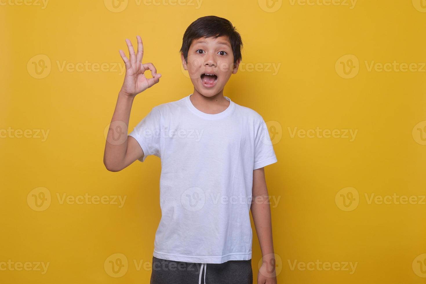 Asian boy in a casual style showing OK sign on a yellow background. The concept of success, approval. Mock up for kids fashion. photo