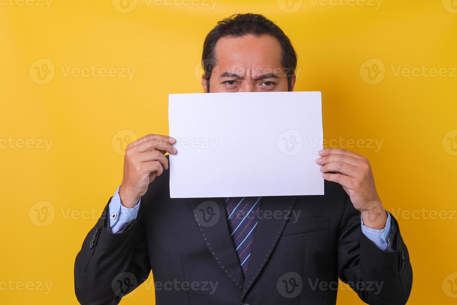 Asian man wearing business suit is frowning and covering half his face  isolated on yellow background. Mock up and copy space. photo