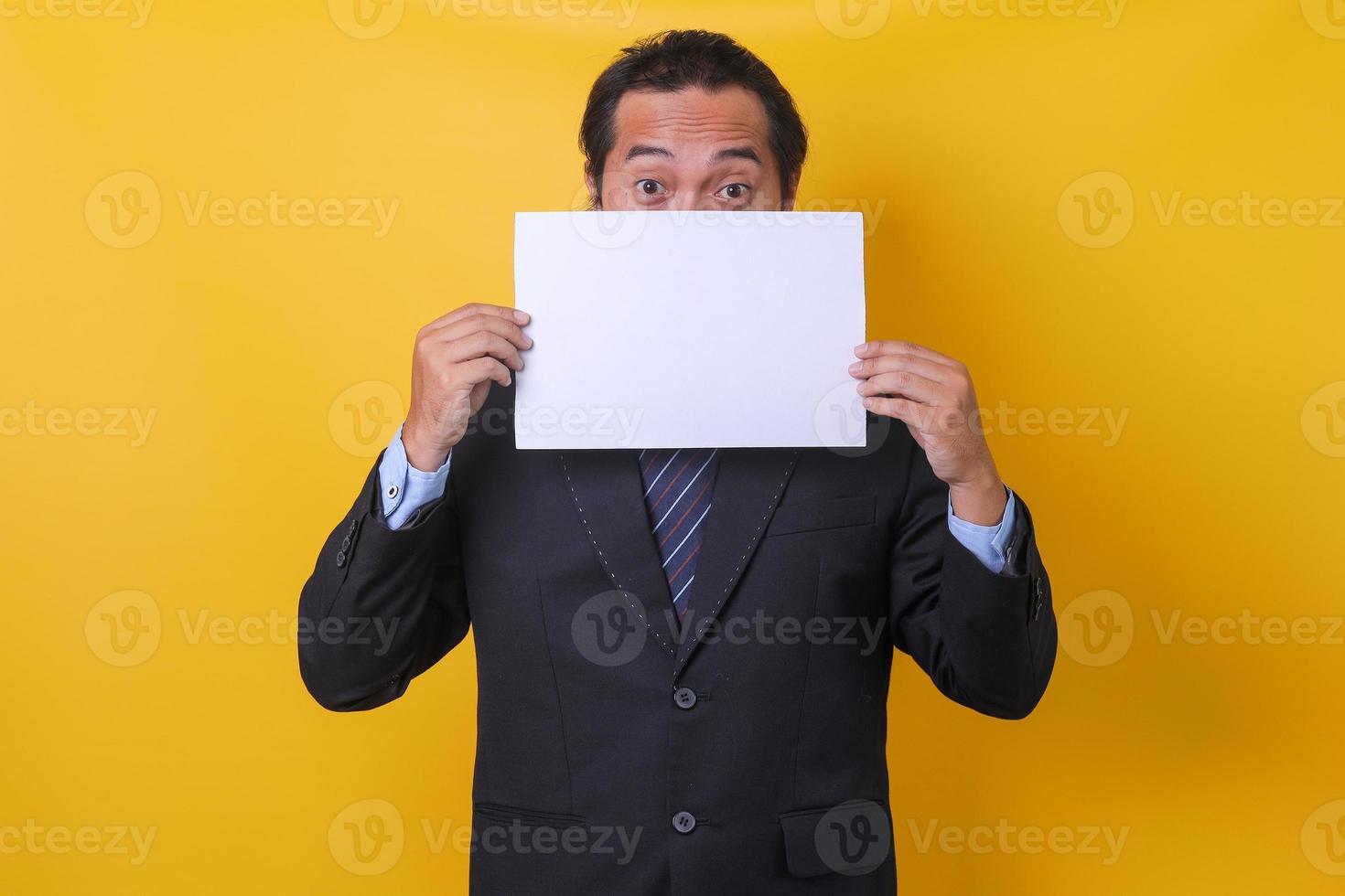 Asian man wearing business suit covering half his face with wide-eyed isolated on yellow background. Mock up and copy space. photo