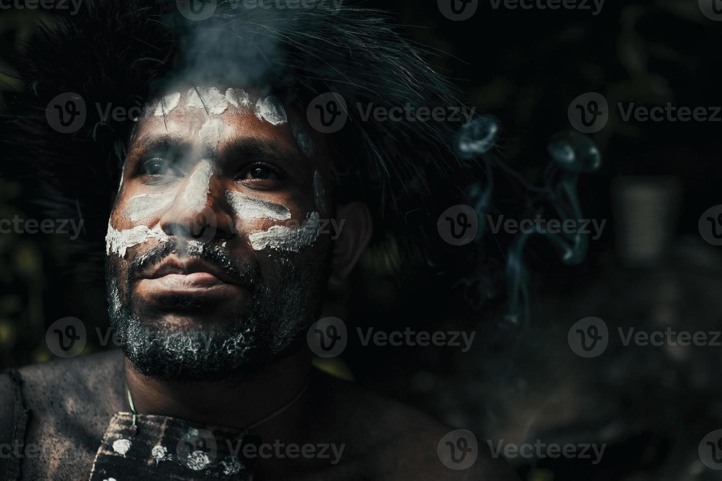 Close-up face of Papua man from Dani tribe blowing the smoke against pure dark background. photo