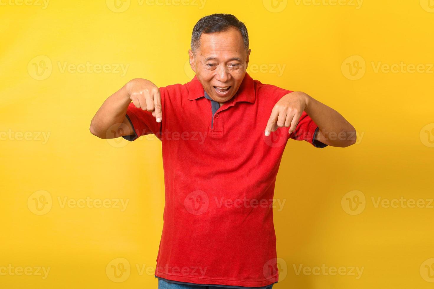 Asian senior man in red t-shirt smiling anf pointing finger down trying to pay attention to important information. photo