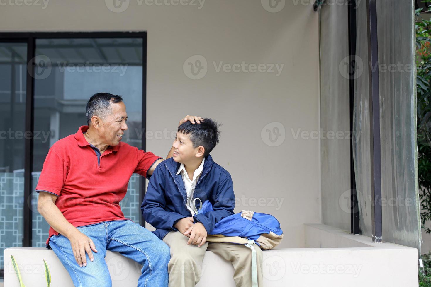 Grandfather sitting and stroking head his grandson, after school in the house yard. Parenting and family activity concept. photo