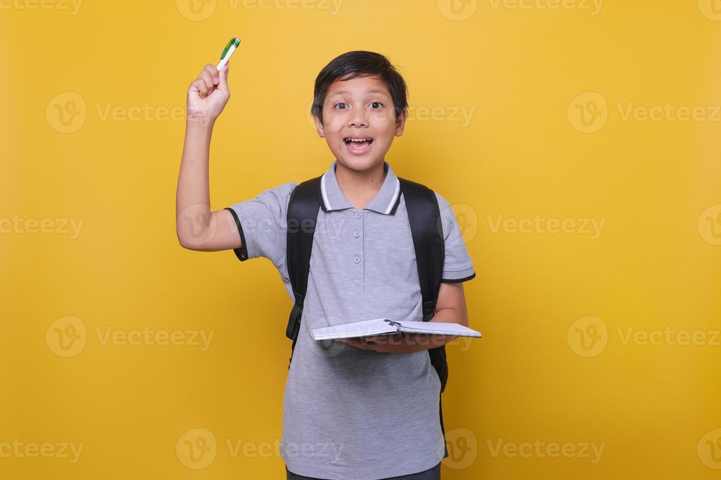 retrato de un escolar asiático con una expresión cuando tiene una idea o una solución, vistiendo un polo gris y sosteniendo un libro y un bolígrafo. concepto de regreso a la escuela. foto