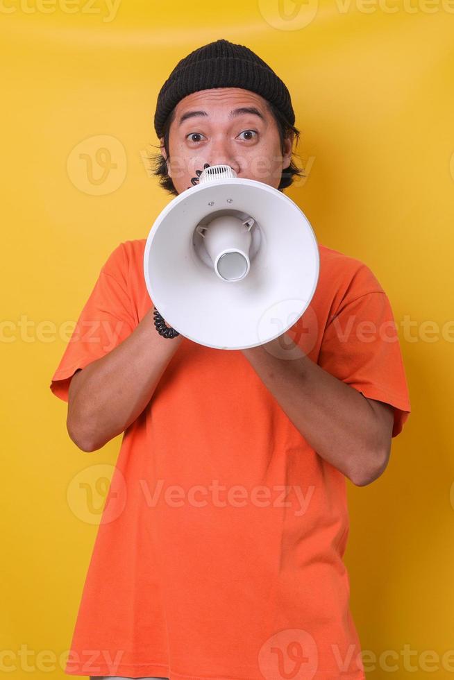 Asian casual guy isolated on yellow background using megaphone with surprised expression. photo