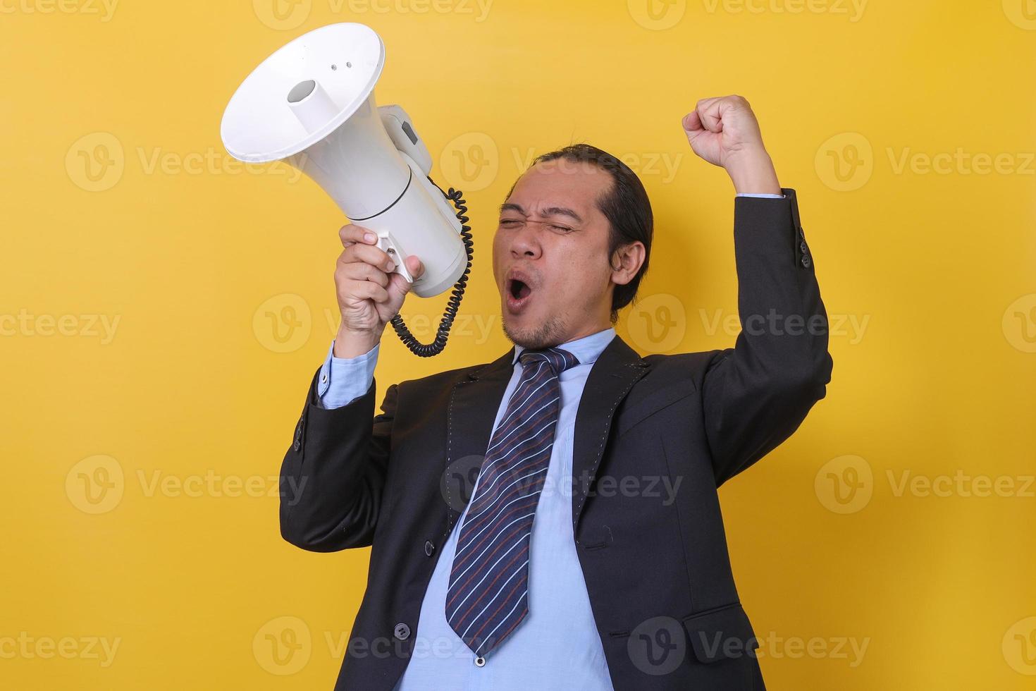 Portrait of a handsome young businessman in suit is screaming and holding megaphone  isolated over yellow background. photo